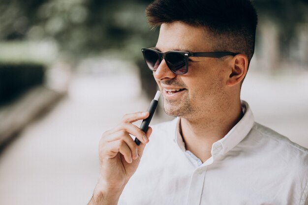 Joven fumando cigarrillo electro afuera en el parque