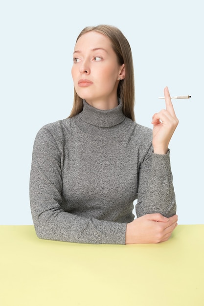 La joven fumando cigarrillos mientras está sentado a la mesa en el estudio.