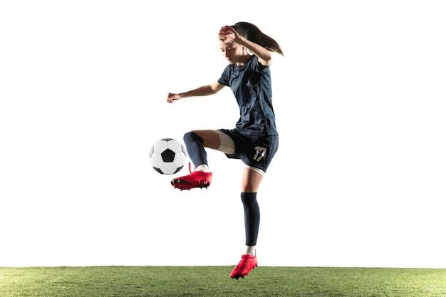 Joven futbolista o futbolista con pelo largo en ropa deportiva y botas pateando la pelota para el gol en salto aislado sobre fondo blanco. Concepto de estilo de vida saludable, deporte profesional, afición.