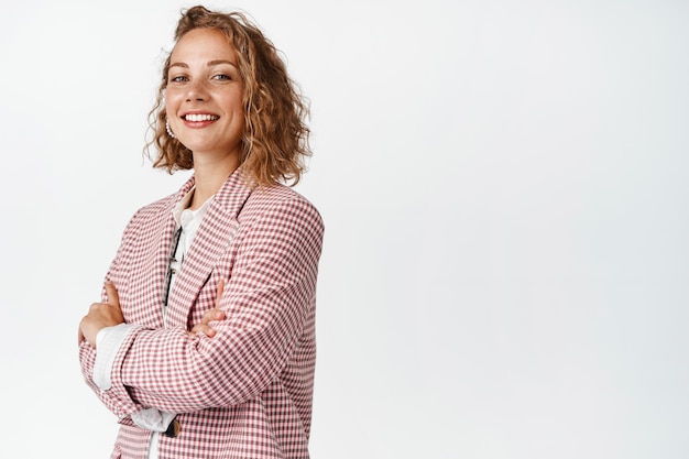 Foto gratuita joven gerente esperanzada, mujer de negocios cruza los brazos en el pecho, sonriendo y luciendo segura como un verdadero profesional, de fondo blanco