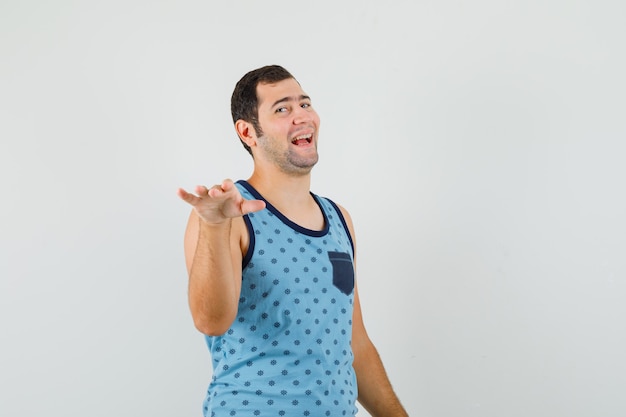 Joven gesticulando con la palma hacia afuera para detenerse en camiseta azul y luciendo divertido.