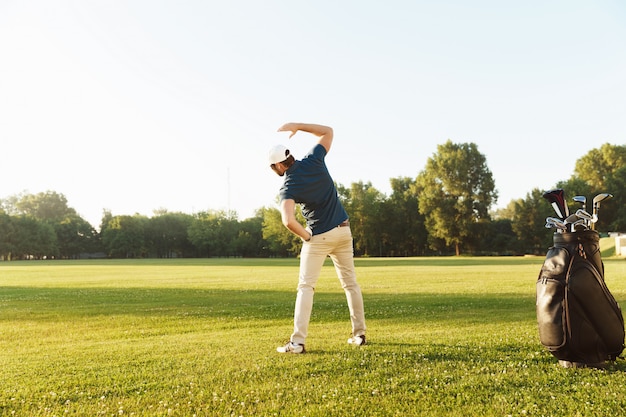 Joven golfista masculino estirando los músculos antes de comenzar el juego