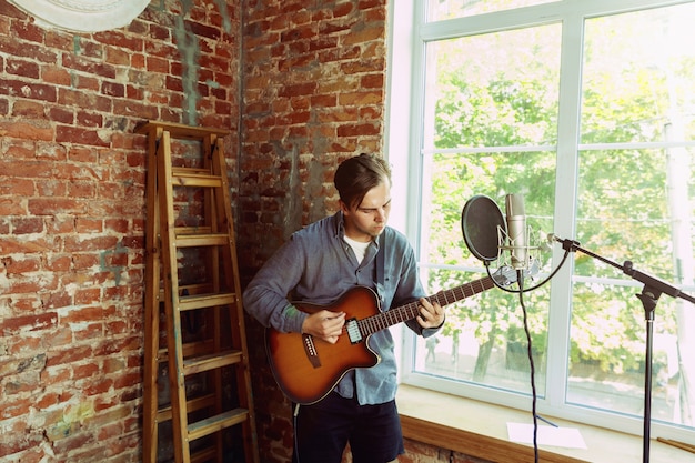 Joven grabando un blog de videos musicales, una lección en casa o una canción, tocando la guitarra o haciendo un tutorial de transmisión por Internet mientras está sentado en el lugar de trabajo del loft o en casa