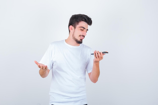 Joven grabando mensajes de voz en el teléfono móvil en camiseta y mirando alegre