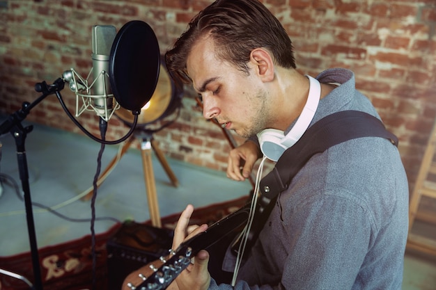 Foto gratuita joven grabando música, tocando la guitarra y cantando en casa