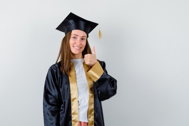 Joven graduada mostrando un golpe en la vestimenta académica y luciendo feliz. vista frontal.