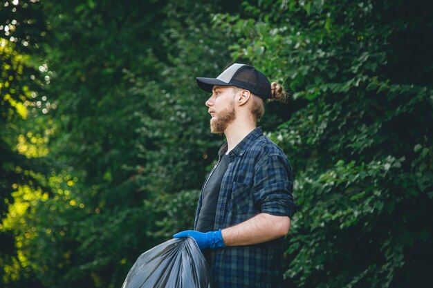 Un joven con guantes y una bolsa de basura limpia en el bosque