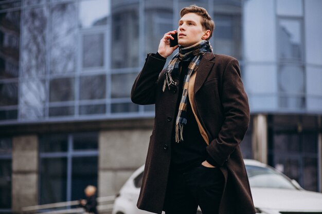 Joven guapo en un abrigo fuera de la calle con teléfono