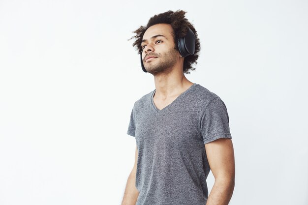 Joven guapo africano escuchando música en auriculares inalámbricos negros