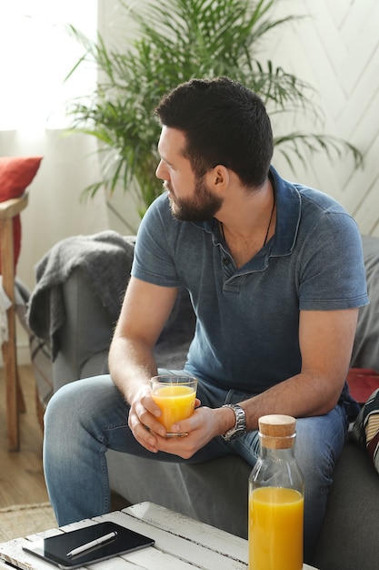 Joven guapo bebiendo jugo de naranja en casa