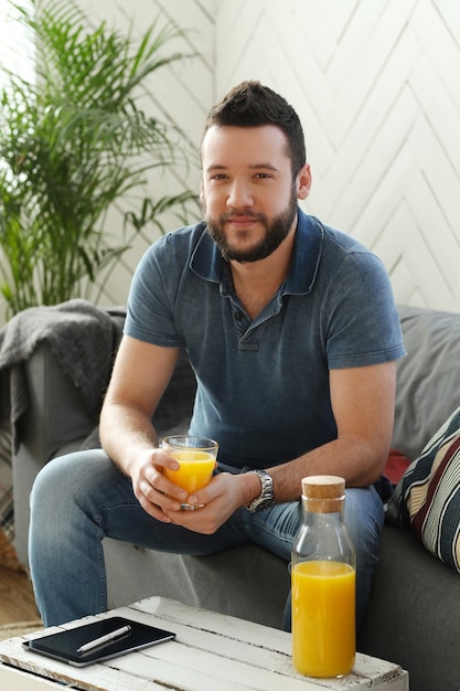 Joven guapo bebiendo jugo de naranja en casa