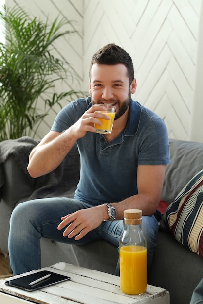 Joven guapo bebiendo jugo de naranja en casa