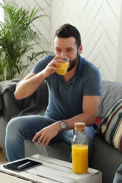 Joven guapo bebiendo jugo de naranja en casa