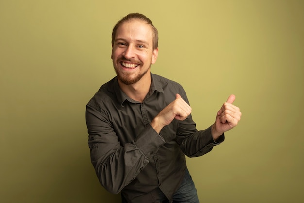 Joven guapo en camisa gris sonriendo alegremente apuntando con los pulgares hacia atrás