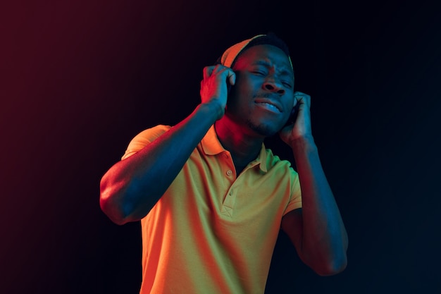 El joven guapo feliz hipster hombre escuchando música con auriculares en estudio negro con luces de neón. Discoteca, club nocturno, estilo hip hop, emociones positivas, expresión facial, concepto de baile