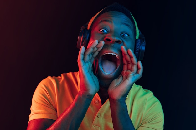 El joven guapo feliz hipster hombre escuchando música con auriculares en estudio negro con luces de neón. Discoteca, club nocturno, estilo hip hop, emociones positivas, expresión facial, concepto de baile