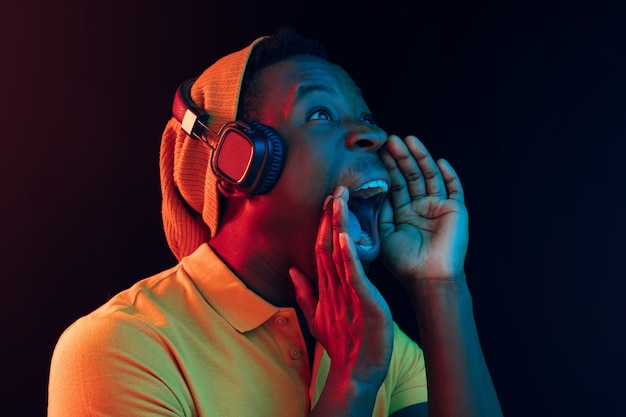 El joven guapo feliz hipster hombre escuchando música con auriculares en negro con luces de neón