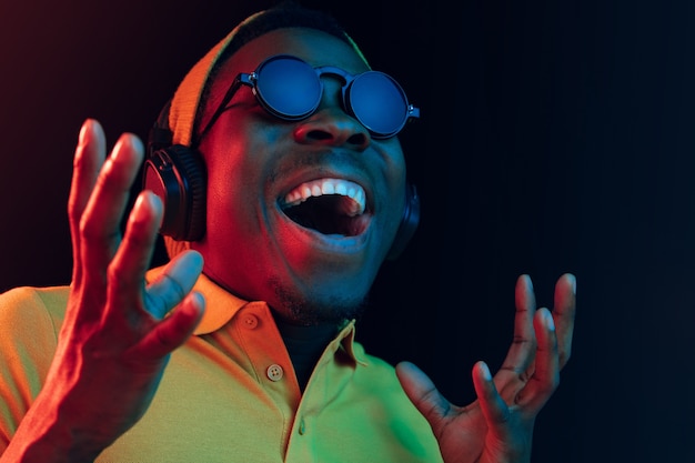 El joven guapo feliz hipster hombre escuchando música con auriculares en negro con luces de neón