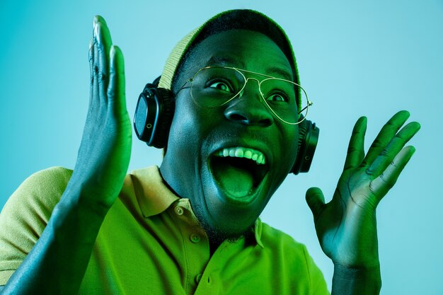 El joven guapo feliz sorprendido hipster hombre escuchando música con auriculares en el estudio con luces de neón.