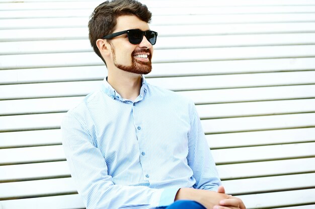 Joven guapo hipster estudiante masculino sentado en el banco en un parque