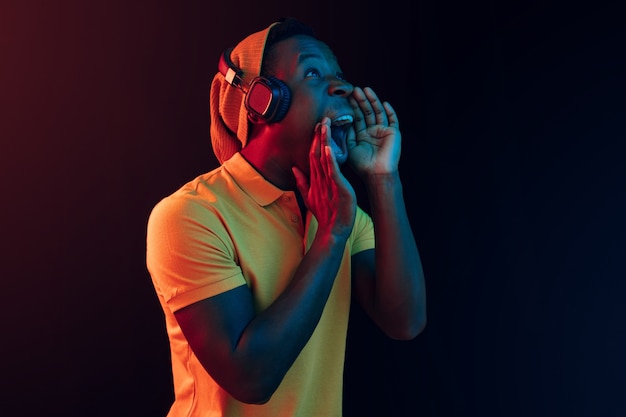 El joven guapo hipster feliz escuchando música con auriculares en el estudio negro con luces de neón. Discoteca, club nocturno, estilo hip hop, emociones positivas, expresión facial, concepto de baile