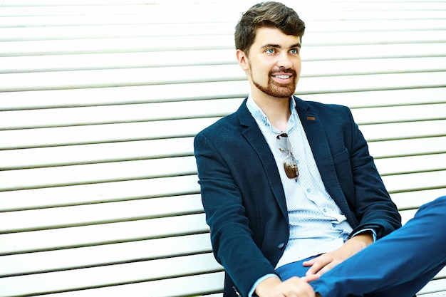 Joven guapo hipster sonriente estudiante masculino sentado en el banco en un parque en traje