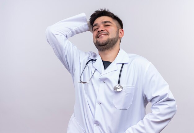 Joven guapo médico con bata médica blanca guantes médicos blancos y un estetoscopio