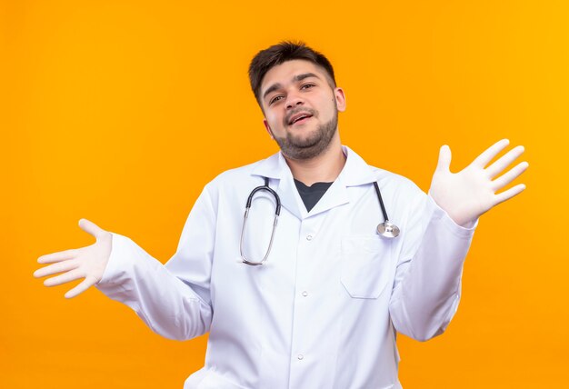 Joven guapo médico con bata médica blanca guantes médicos blancos y un estetoscopio