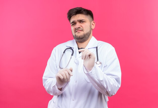 Joven guapo médico con bata médica blanca guantes médicos blancos y un estetoscopio