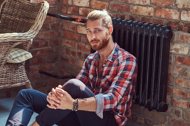 Foto gratuita un joven y guapo modelo pelirrojo se sienta en el suelo de la habitación con un interior tipo loft.