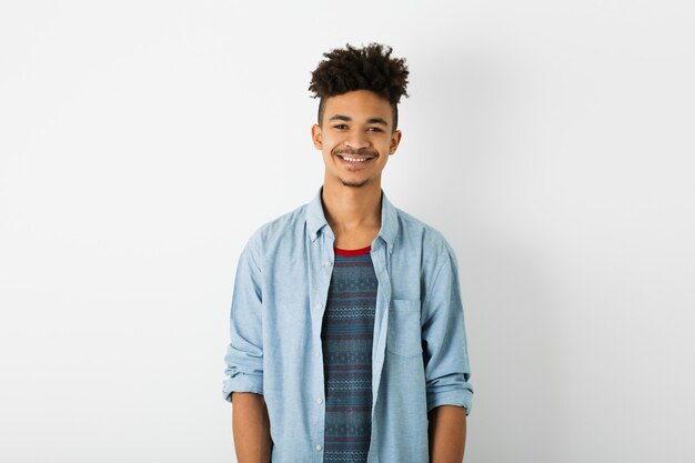 Joven guapo negro, expresión de la cara sonriente, mirando a puerta cerrada, estado de ánimo positivo, emoción feliz, aislado sobre fondo blanco de estudio, juventud afroamericana, estilo hipster, estudiante, camisa azul