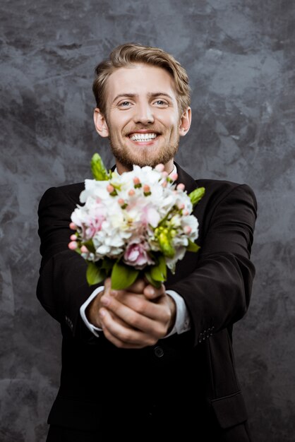 Joven guapo novio sonriendo, con ramo de novia