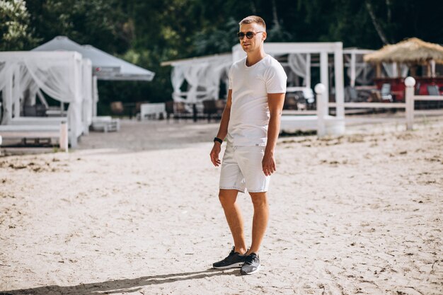 Joven guapo parado en la playa por el parque