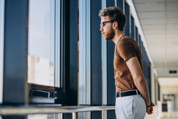 Joven guapo de pie junto a la ventana en el aeropuerto