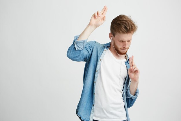 Joven guapo positivo en auriculares escuchando música bailando en movimiento.