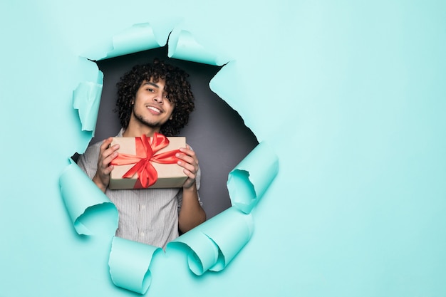 Joven guapo rizado con regalo de agujero en papel verde