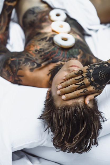 joven guapo tatuado desayunando en la cama al aire libre al aire libre en el jardín