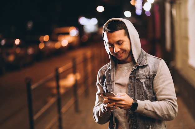 Joven guapo con teléfono por la noche en la calle