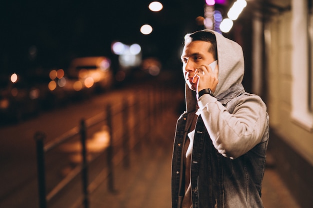 Joven guapo con teléfono por la noche en la calle