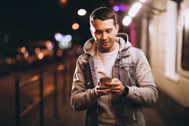 Joven guapo con teléfono por la noche en la calle