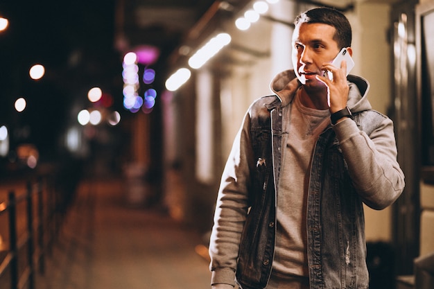 Joven guapo con teléfono por la noche en la calle