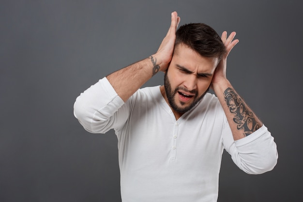 Joven guapo tiene dolor de cabeza sobre la pared gris