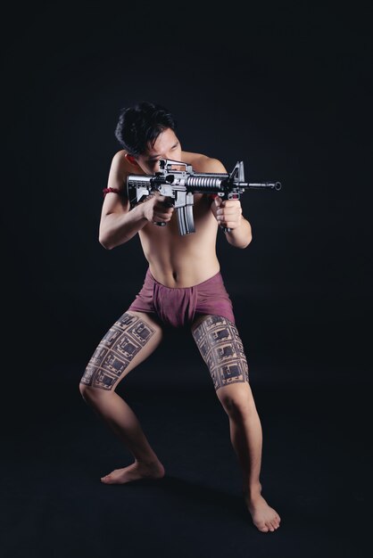 Joven guerrero masculino de Tailandia posando en una posición de combate con un arma de fuego