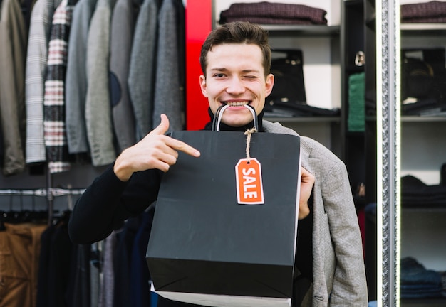 Joven guiñando sus ojos con bolsas de compras en la boca