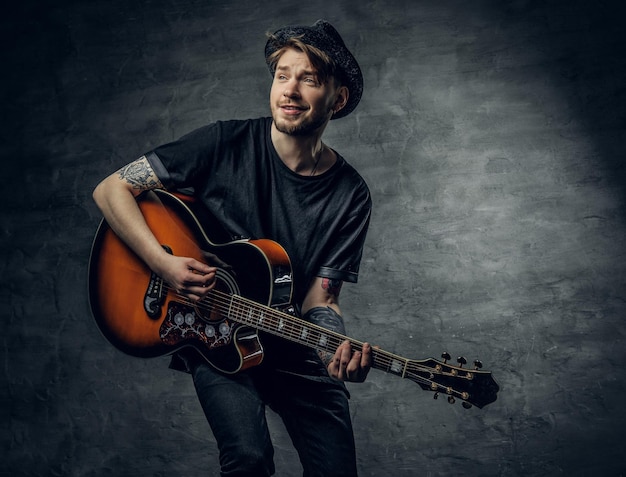 Joven guitarrista acústico de jazz y blues hipster de moda con tatuajes en los brazos tocando la melodía.