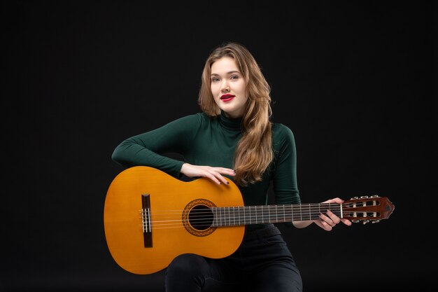 Joven guitarrista femenina motivada sosteniendo su instrumento musical favorito en la oscuridad