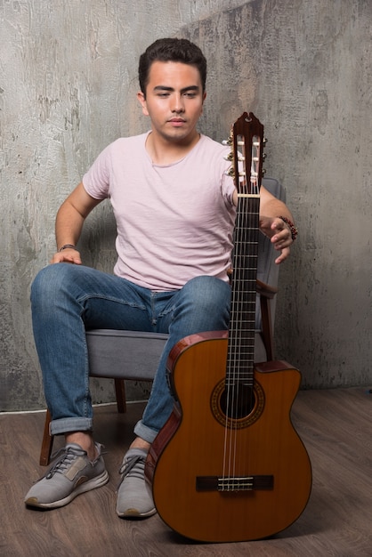 Joven guitarrista sosteniendo la guitarra sobre fondo de mármol