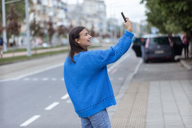 Una joven hace un selfie con la cámara del teléfono en la calle.