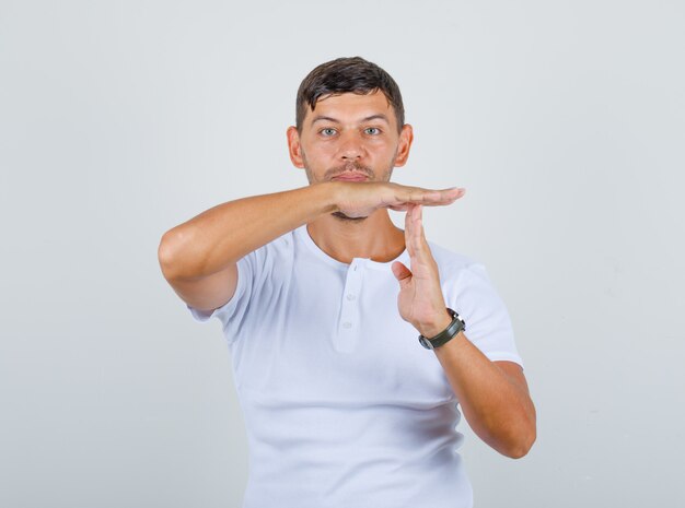 Joven haciendo gesto de descanso de tiempo en camiseta blanca, vista frontal.