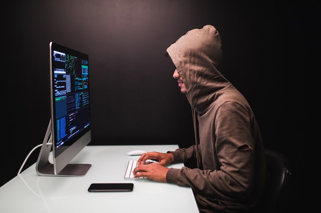 Foto gratuita joven hacker masculino en el cuarto oscuro escribiendo código o usando un programa de virus informático para un ataque cibernético